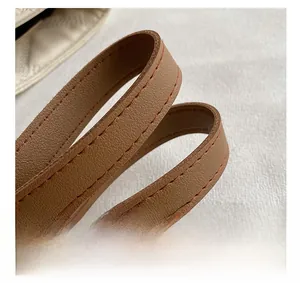 Detail of brown leather strap with orange stitching on minimalist beige tote bag