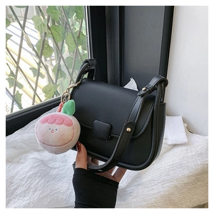 Détail d'un sac bandoulière noir avec un pendentif en peluche pêche sur fond blanc