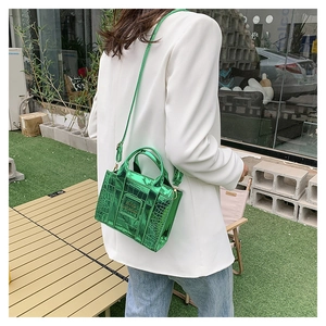 Detail of green crocodile embossed handbag worn with a white blazer in a street scene