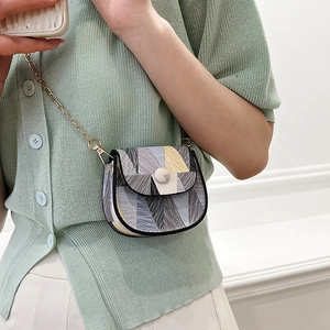 Mini geometric patchwork crossbody bag with gold chain strap on a green knit cardigan