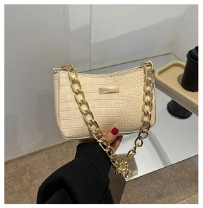 Detail of beige crocodile pattern handbag with elegant chunky gold chain strap decoration