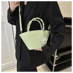 Detail of mint green handbag with woven handles and a decorative white floral charm