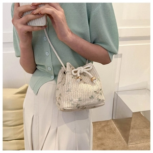 Détail d'un sac seau tressé beige avec broderies florales vertes et cordon de serrage