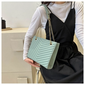 Detail view of mint green quilted tote bag with golden metal chain strap on model