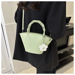 Detail view of avocado green tote bag with braided handle and floral charm on a model