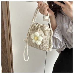 Detailed view of beige woven bucket bag with large white knit flower and drawstring strap