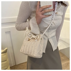 Close-up of cream woven bucket bag with drawstring closure and golden metal details