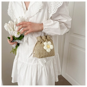 Detail view of woven straw bucket bag with a white crochet flower and drawstring