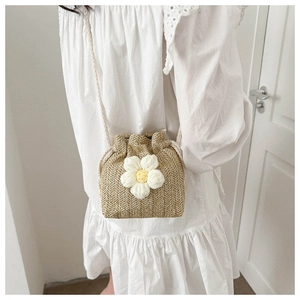 Detail of woven straw bucket bag featuring a large 3D white knitted flower decoration