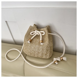 Detail of woven straw bucket bag showing herringbone texture and white drawstring tassels