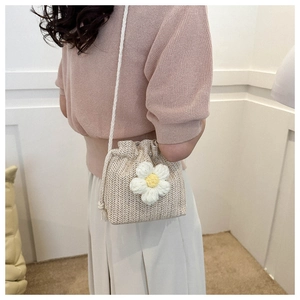 Detailed view of handmade woven straw bucket bag with white daisy flower and strap
