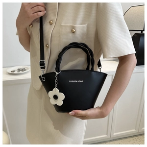 Close-up of black leather bucket bag with woven handles and white floral charm detail
