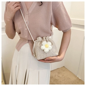 Detail of hand-woven beige bucket bag featuring a white floral ornament and drawstring closure