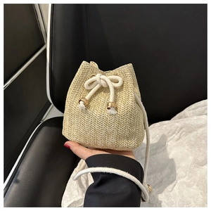 Close-up of beige woven straw bucket bag with white drawstring and gold metal hardware