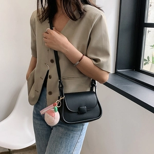Sac bandoulière noir minimaliste avec breloque pêche dans un décor intérieur épuré