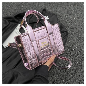 Macro detail of metallic pink crocodile pattern tote bag with gold brand lettering