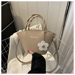 Beige tote bag with woven handles and flower charm displayed on a white blazer