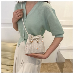 Detail of woven straw bucket bag featuring daisy embroidery and cotton drawstring closure