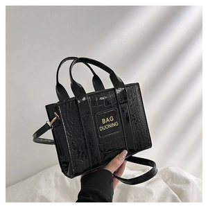 Detail of black crocodile-embossed patent leather handbag with gold logo lettering