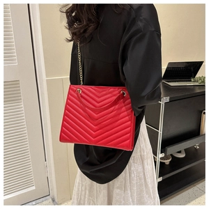 Detail of red V-quilted tote bag with leather handles and gold metal chain strap