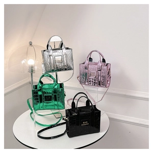 Detail showing four colors of glossy crocodile pattern crossbody bags on white display stand