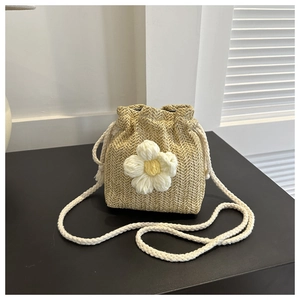Detail of hand-woven straw bucket bag featuring a large white crochet flower charm