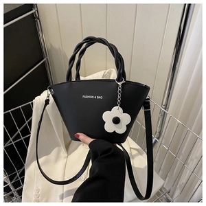 Detail of black leather bucket bag featuring woven handle and white flower charm in a basket