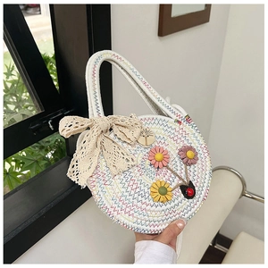 Détail du sac à main rond en paille avec fleurs colorées et grand nœud en dentelle