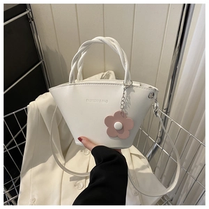 Detail of white semi-circular handbag with woven handle, shoulder strap and flower charm