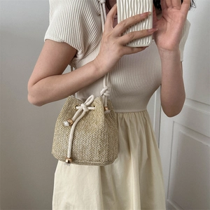 Minimalist beige woven straw bucket bag with drawstring closure and golden bead details
