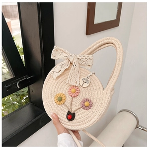 Détail du sac à main rond en paille avec broderies florales et nœud en dentelle blanche