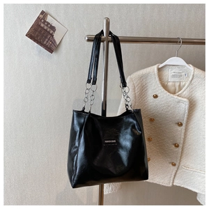 Détail d'un sac cabas noir brillant avec lanières en chaîne argentée et étiquette