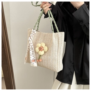 Detail of hand-woven straw tote with green handle and decorative floral pendant