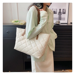 Detailed view of a white quilted tote bag with brown straps worn by a model in a room