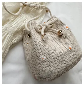 Detail of beige woven bucket bag featuring daisy embroidery and drawstring closure