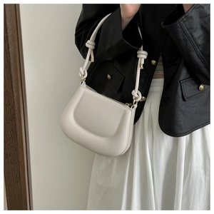 Close-up of beige leather shoulder bag with decorative knotted strap and gold hardware