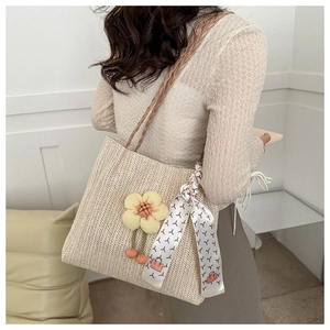 Detail of woven straw tote bag with floral pendant and patterned silk scarf on handle