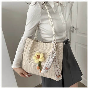 Detail of beige woven tote bag featuring yellow floral charm and printed silk scarf handle