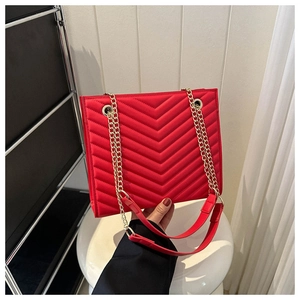 Detail of red quilted tote bag featuring golden chain strap and chevron texture