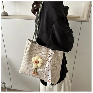 Close-up of woven straw tote bag with yellow floral charm and green rope shoulder strap
