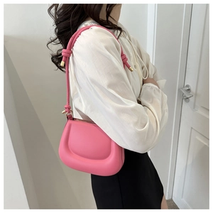 Pink matte leather shoulder bag with decorative knotted strap shown on model outfit