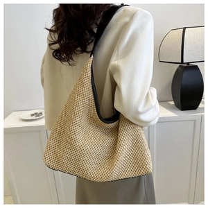 Détail d'un sac hobo en paille tressée avec bordure en cuir noir porté à l'épaule