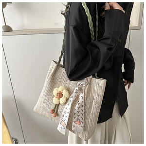 Detail of woven straw tote bag featuring floral pendant and colorful silk scarf detail