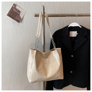Détail du sac cabas beige avec chaîne argentée et étiquette logo carrée élégante