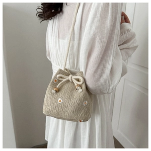 Detail of woven straw bucket bag featuring delicate white daisy embroidery and drawstring closure