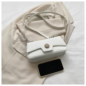 Close-up of white minimalist baguette bag next to a smartphone for size comparison