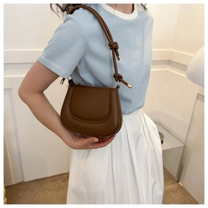 Detail of a brown matte leather saddle bag featuring a textured flap and knotted strap details