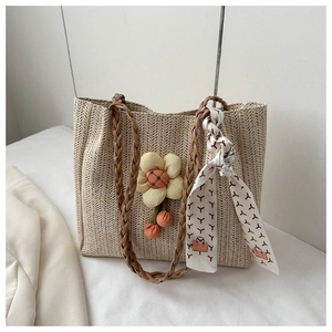 Detail of beige straw tote bag with woven handles, flower charm and printed silk scarf