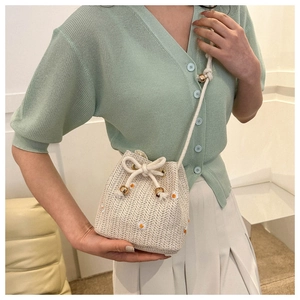 Detailed side view of woven straw bucket bag with floral embroidery and drawstring strap