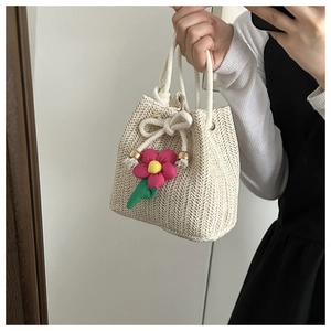 Detail of straw bucket bag with drawstring closure and handmade pink floral ornament